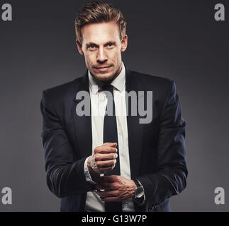 Pensive attractive businessman adjusting his cuff on his shirt as he stands looking at the camera with a quiet smile, upper body Stock Photo