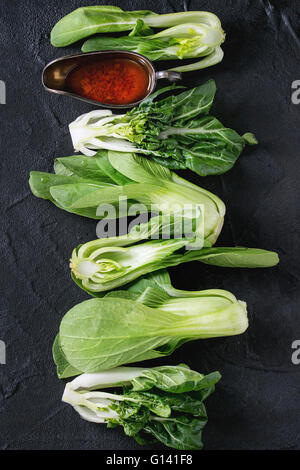 Assortment of whole and sliced raw baby bok choy (Chinese cabbage) and chili pepper olive oil over old black textured background Stock Photo