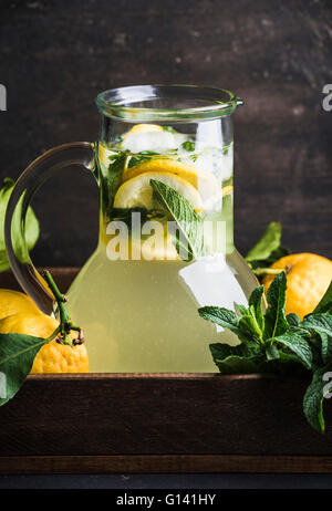 Homemade lemonade with mint and ice, served with fresh lemons in wooden tray, copy space. Dark background Stock Photo