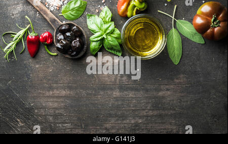 Food background with vegetables, herbs and condiment. Greek black olives, fresh basil, sage, rosemary, tomato, peppers, oil on d Stock Photo
