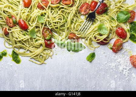 Spaghetti with pesto sauce, roasted cherry-tomatoes, fresh basil and parmesan cheese on steel backdrop. Top view, copy space Stock Photo