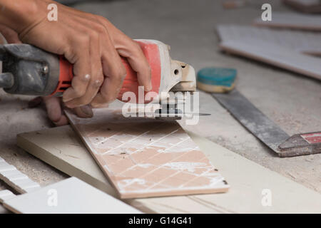 worker grinding a tile using an angle grinder at construction site Stock Photo