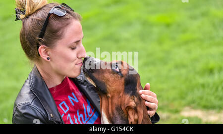 Young woman with an affectionate one year old Basset hound (Canis lupus familiaris) in the yard of a hobby farm. Stock Photo