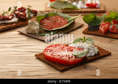 Bread crisp (crispbread open-faced sandwich) with heirloom tomato, cream cheese and fresh basil leaves on wooden table. Selectiv Stock Photo