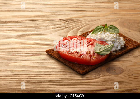 Bread crisp (crispbread open-faced sandwich) with heirloom tomato, cream cheese and fresh basil leaves on wooden table. Infinite Stock Photo