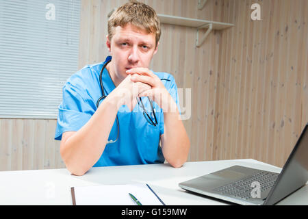 tired Doctor holds in hands glasses sitting at the table Stock Photo