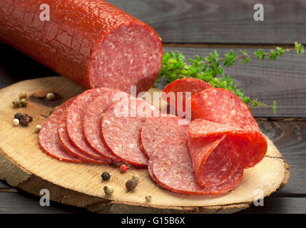 halved in slices turkey salami served on a slice of wood with thyme and ground pepper Stock Photo