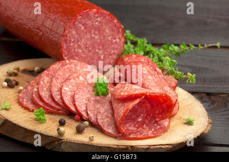 halved in slices salami served on a slice of wood with thyme and ground pepper Stock Photo