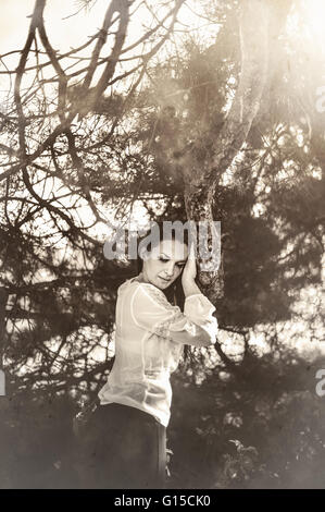 thoughtful woman standing and holding on tree Stock Photo