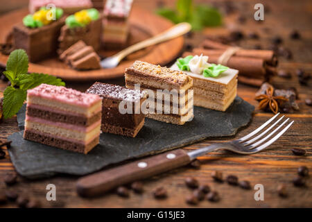 Small square cakes with different cream on black slate Stock Photo