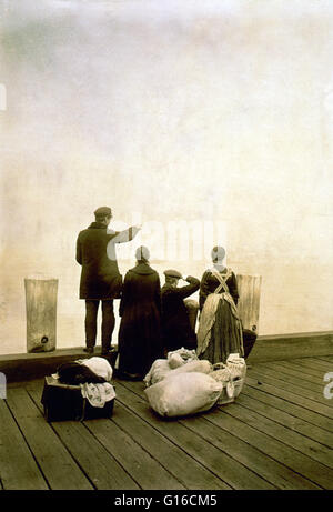 Entitled: 'Four immigrants and their belongings, on a dock, looking out over the water; view from behind.' In the 35 years before Ellis Island opened, over eight million immigrants arriving in New York had been processed by New York State officials at Cas Stock Photo