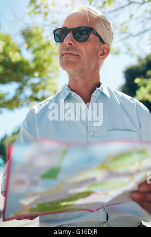 Close up shot of a mature man with a map while standing outdoors in the city on a summer day. Tourist holding a city map and loo Stock Photo