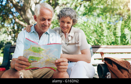 Happy mature couple using city map for direction. Retired couple on a vacation sitting outdoors on a park bench and reading a ma Stock Photo