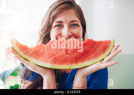 Portrait of happy young woman holding a slice of watermelon in front of her face.