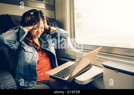 Asian college girl frustrated with laptop on the train, warm light tone, with copy space Stock Photo