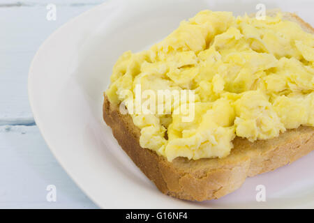 Scrambled eggs on toast in white plate on blue table Stock Photo