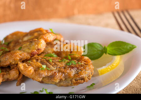Fried pork brain with lemon and herbs on white plate Stock Photo
