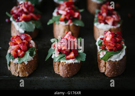 A group of strawberry bruschettas with ricotta cheese and arugula are photographed from the front Stock Photo