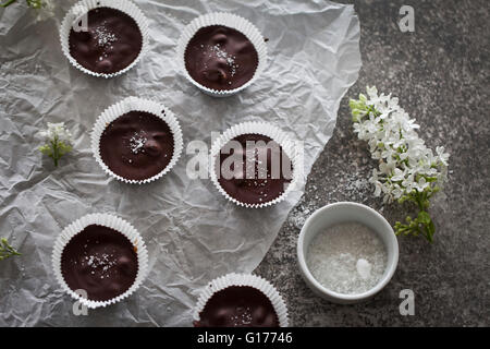 Chocolate cups filled with date caramel with sea salt on a white paper and grey background Stock Photo