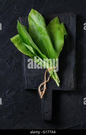 Bunch of fresh ramson on wooden chopping board over black textured background. Top view Stock Photo