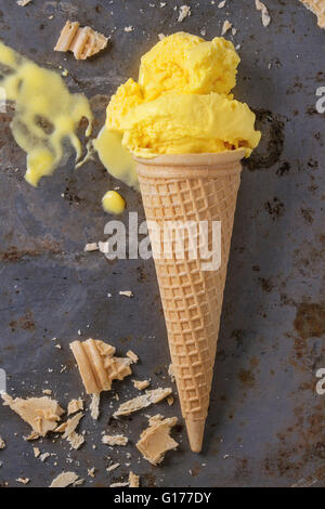 Homemade mango ice cream in waffle cone with wafer crumb over rusty metal textured background. Top view Stock Photo