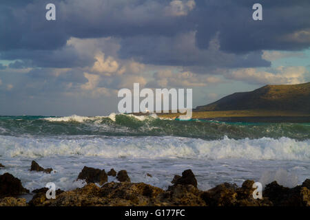 Waves breaking on the rocky shore of the Greek island Kefalonia, in the distance a lighthouse Stock Photo