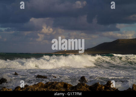 Waves breaking on the rocky shore of the Greek island Kefalonia, in the distance a white lighthouse Stock Photo