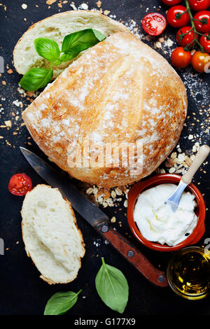 Homemade bread loaf and fresh ingredients for making sandwiches (tomatoes, basil, olive oil, cream cheese) on rustic dark backgr Stock Photo