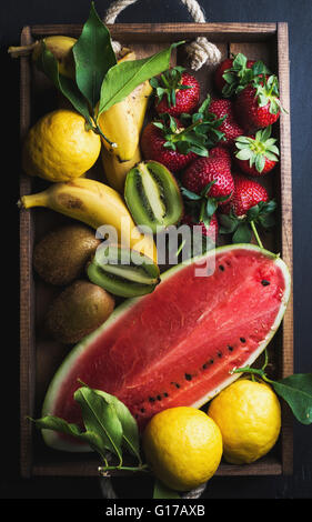 Various colorful tropical fruit selection in wooden tray over dark background, top view. Watermelon, strawberry, lemons and kiwi Stock Photo