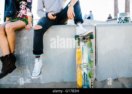 Young couple sitting on wall, man resting foot on skateboard, low section Stock Photo