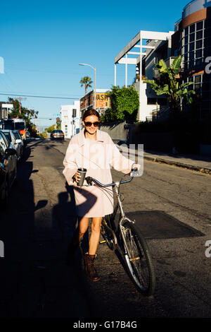 Young stylish woman pushing cycle along street , Venice Beach, California, USA Stock Photo