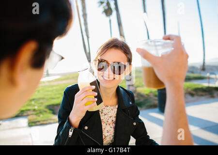 Over shoulder view of young couple raising a juice and coffee toast, Venice Beach, California, USA Stock Photo