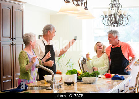 Senior couple taking photograph of friends in kitchen Stock Photo