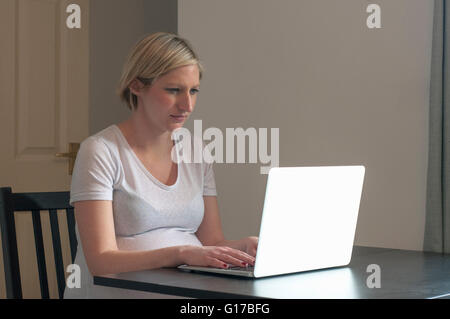 Pregnant woman sitting at table, using laptop computer Stock Photo