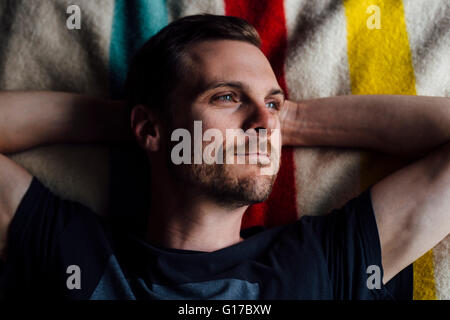 Overhead portrait of handsome man lying on striped blanket with hands behind head Stock Photo