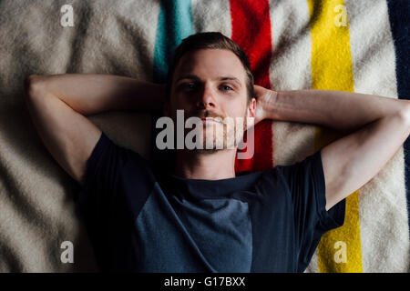 Overhead portrait of confident man lying on striped blanket with hands behind head Stock Photo