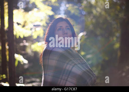 Woman wrapped in checkered shawl in forest Stock Photo