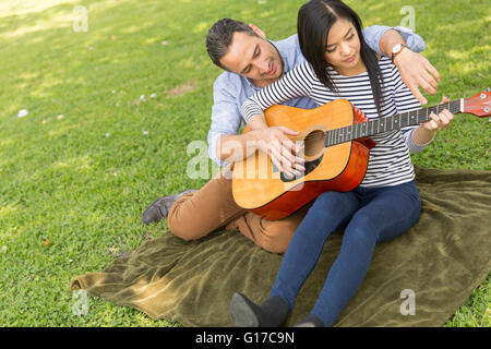 Man sitting on grass teaching woman to play acoustic guitar Stock Photo