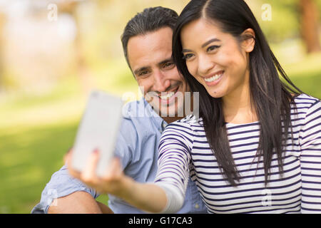 Couple sitting on grass using smartphone to take selfie Stock Photo