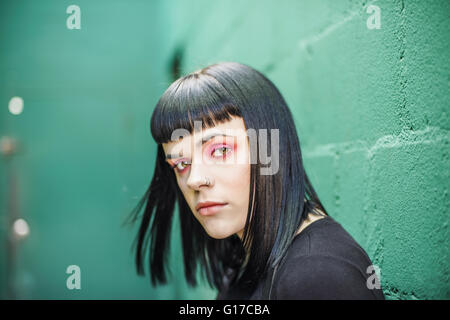 Portrait of woman leaning against painted breeze block wall looking at camera Stock Photo
