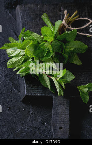 Bunch of fresh mint with thread on black wooden chopping board over black textured background. Stock Photo