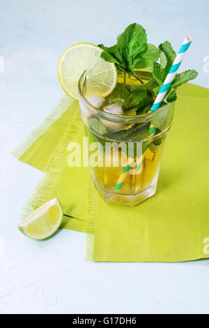 Glass of Iced green tea with lime, lemon, mint and ice cubes on green textile napkin over light blue textured background. Stock Photo