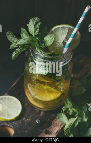 Ice green tea with ice, fresh mint, lime and lemon in glass mason jar with retro cocktail tube, served on wooden chopping board Stock Photo