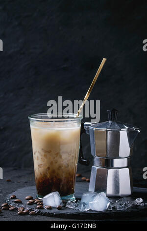 Glass of ice coffee with cream and milk, served with coffee beans, ice cubes and coffee pot on slate stone board over black text