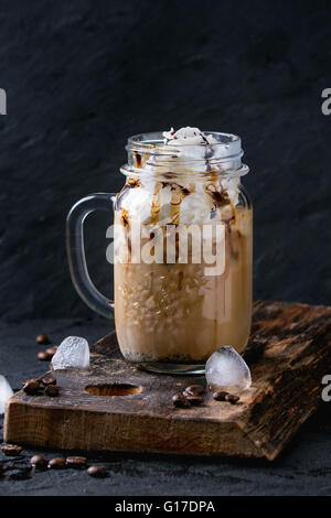 Glass mason jar with ice coffee with whipped cream, ice cream and chocolate sauce, served with coffee beans and ice cubes on woo Stock Photo