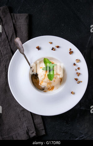 White ceramic plate with caramel and Hazelnut butter Ice cream, served with caramel syrup, silver spoon, mint and crispy nuts on Stock Photo