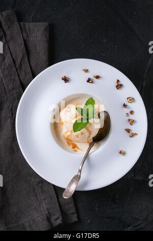 White ceramic plate with caramel and Hazelnut butter Ice cream, served with caramel syrup, silver spoon, mint and crispy nuts on Stock Photo