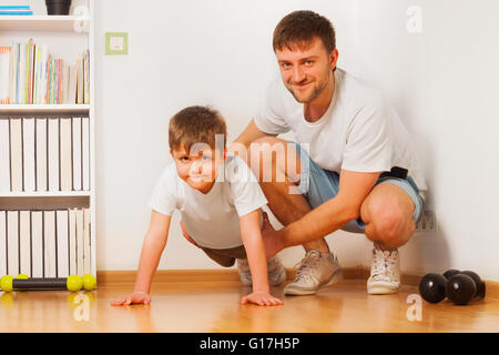 Father helping his kid son doing press-ups at home Stock Photo