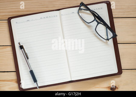Office workplace with notebook, eye glasses and pen on rustic wood table.Top view Stock Photo