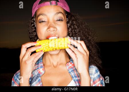 Young woman biting corn on the cob looking at camera Stock Photo